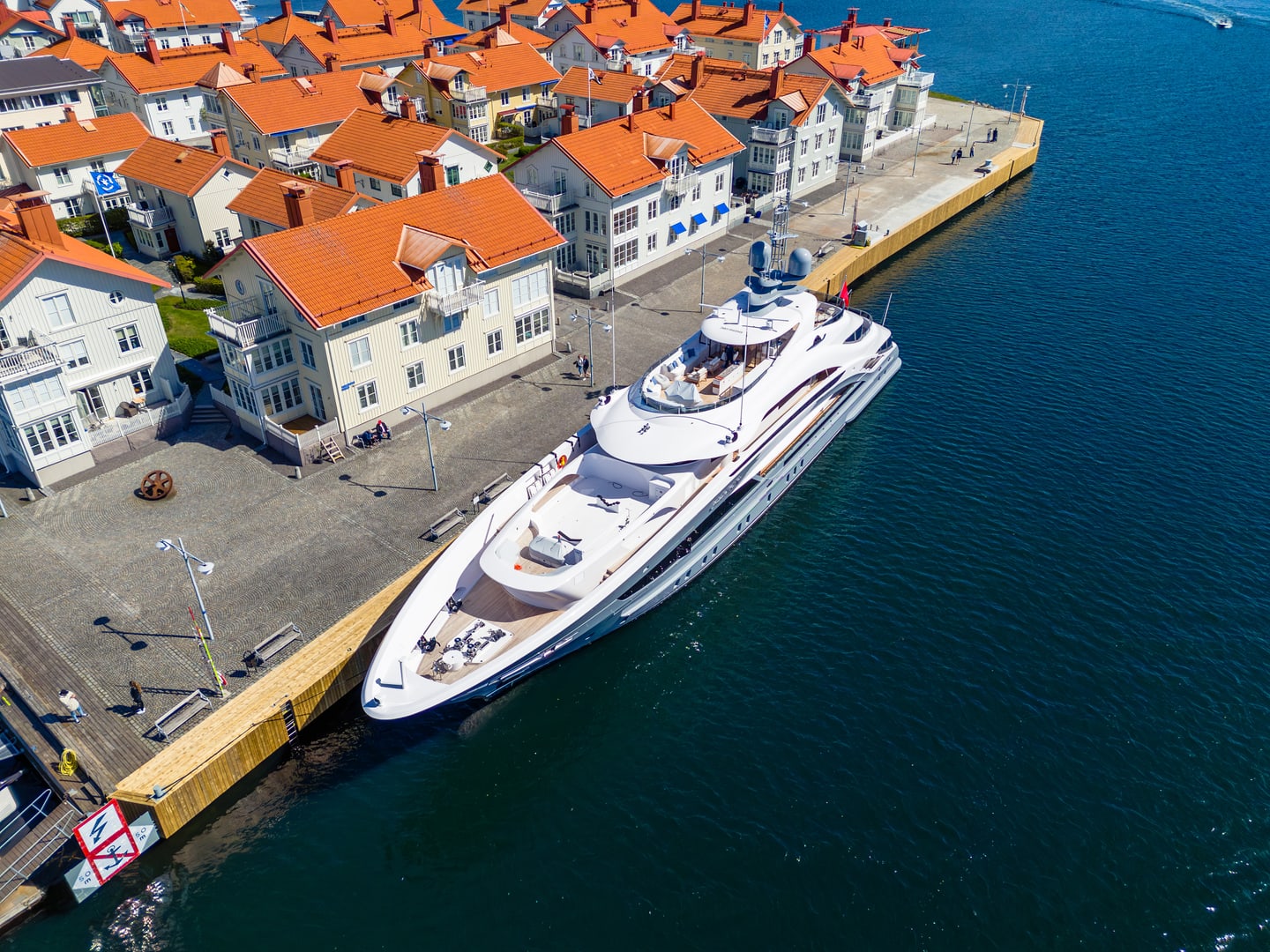 A large white yacht moored beside red-roofed harbor buildings.