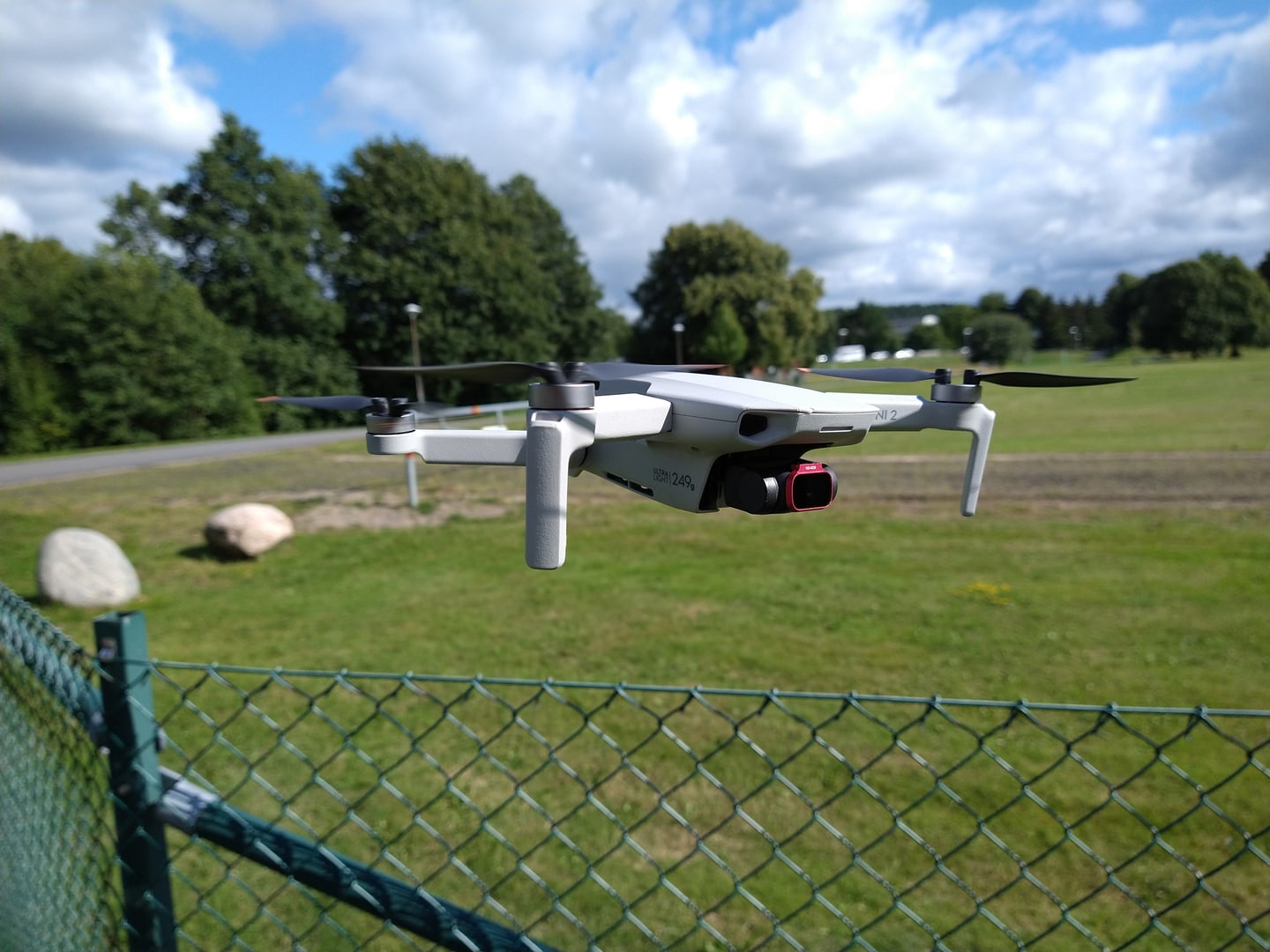 A DJI Mini 2 drone hovering above a fence by a grassy field.