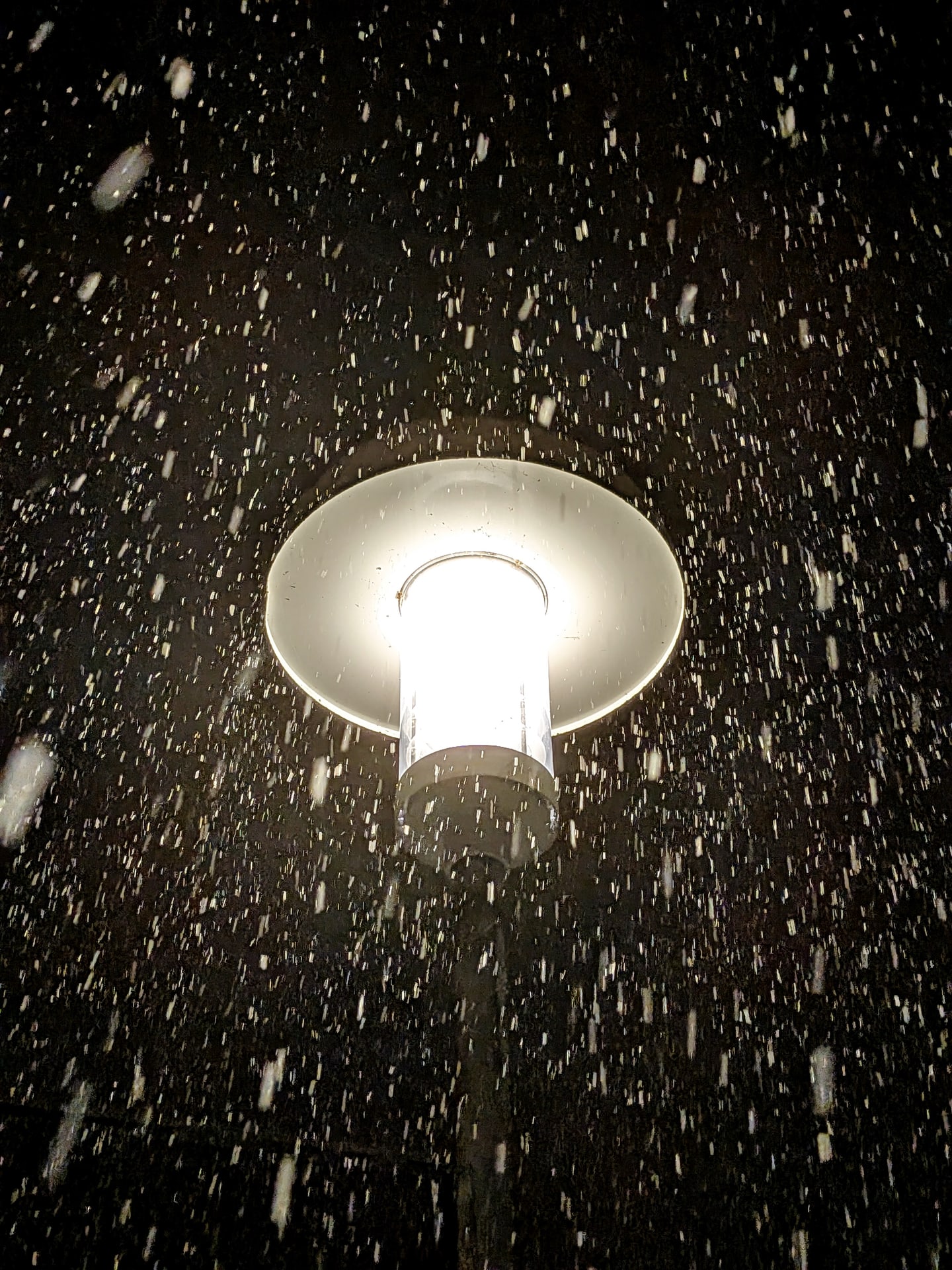 Snow falling through the glow of a bright outdoor lamp at night.