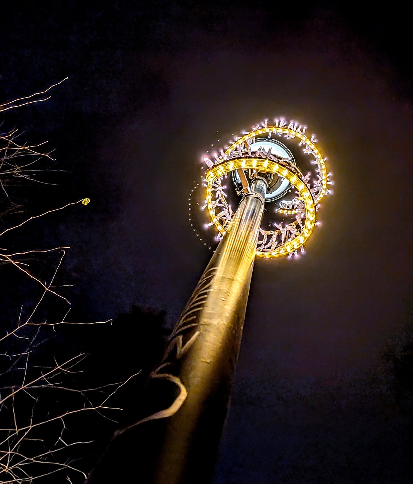 A tall pole with a bright circular light installation against a dark night sky.