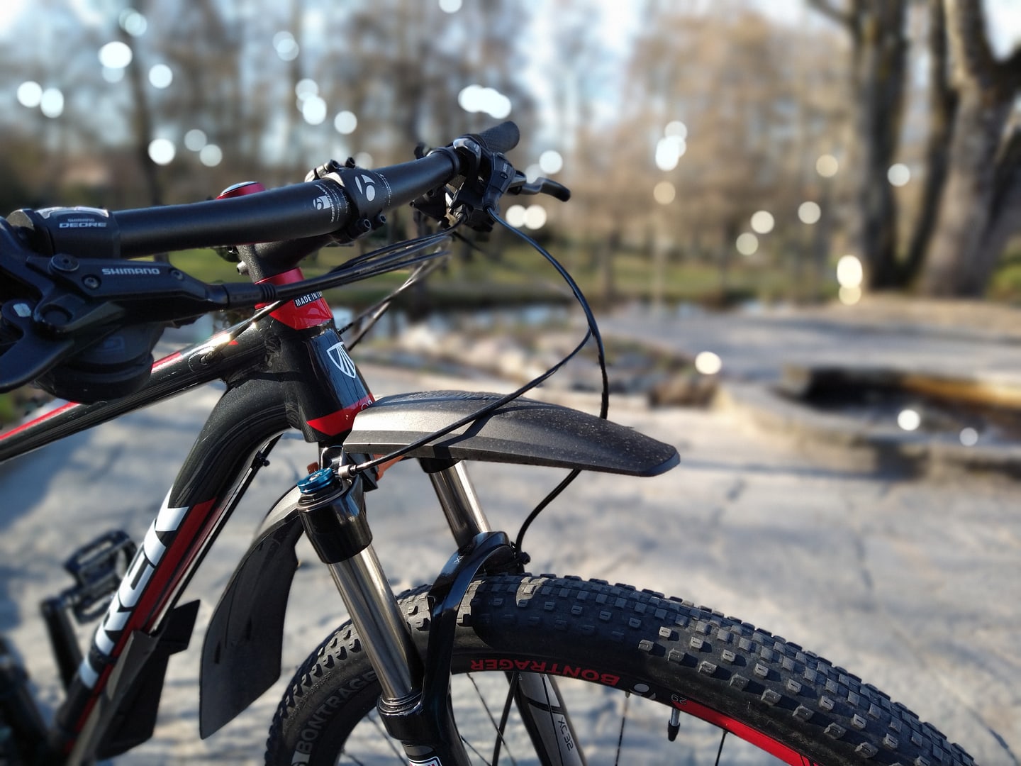 Close-up of a mountain bike front wheel and handlebar by the water.