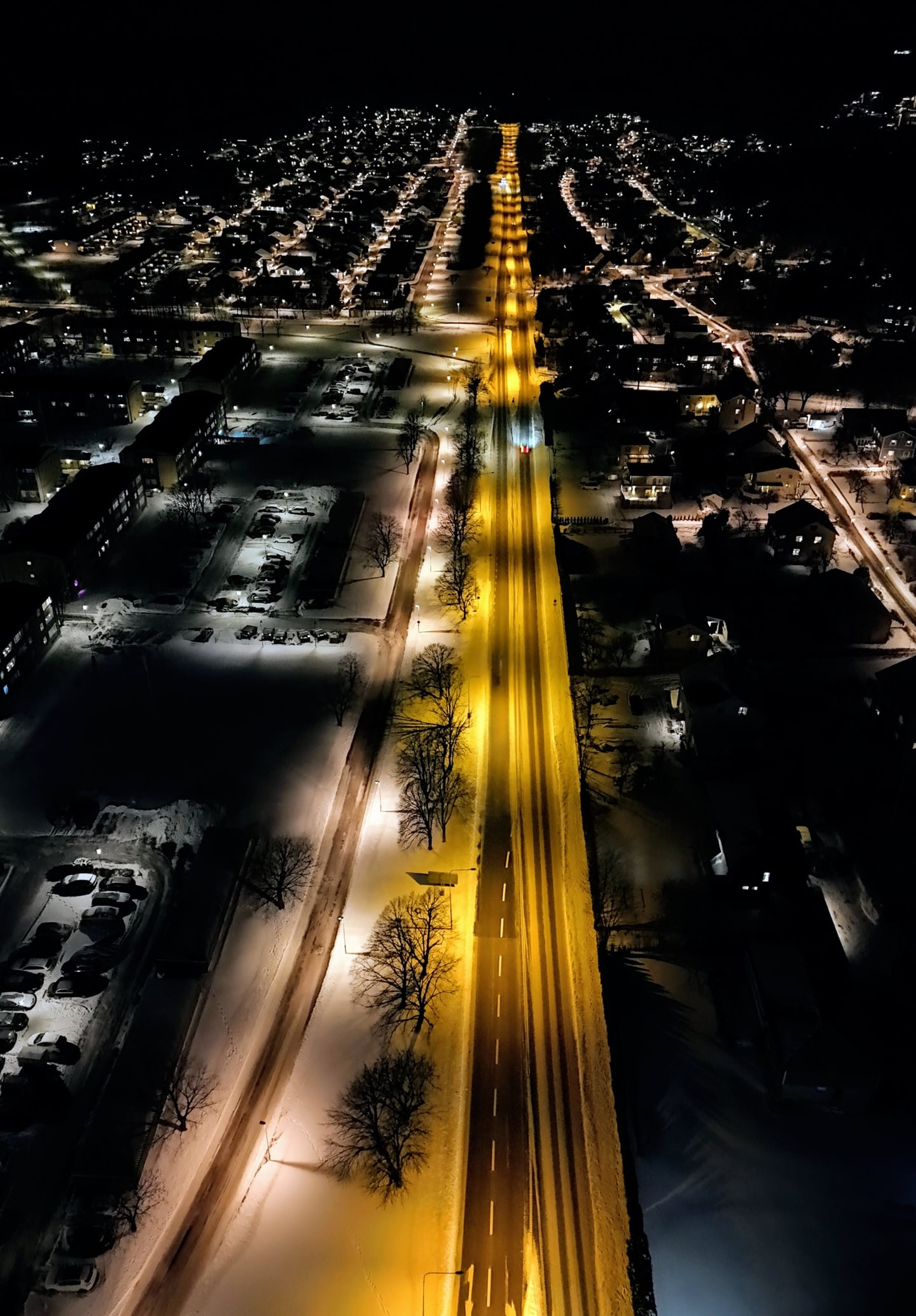 A night aerial view of a lit road stretching through dark surroundings.