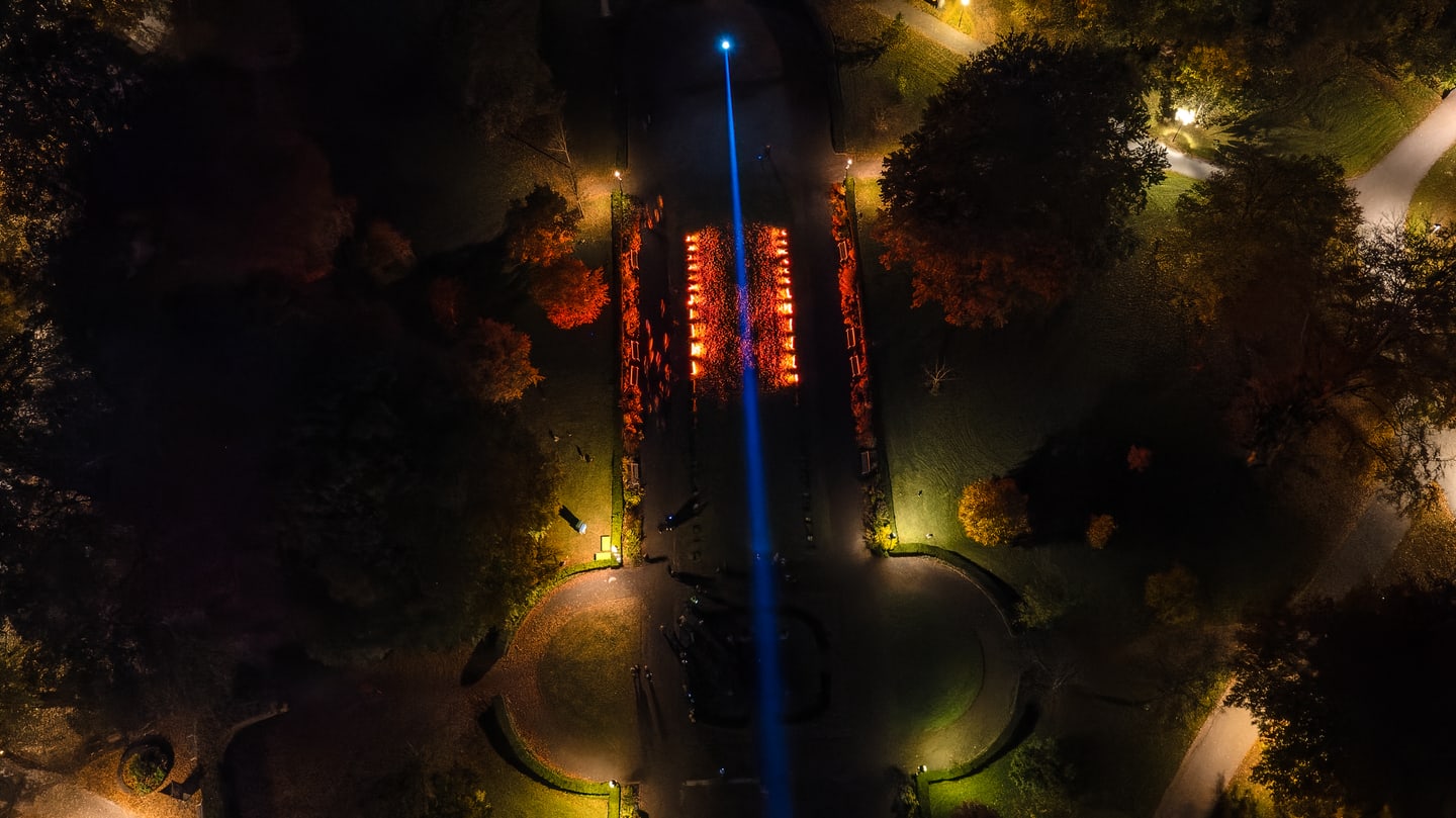 Night aerial view of a park light installation with a bright blue beam running through the center.