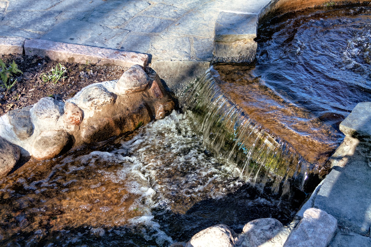 A small stepped waterfall flowing over stonework in bright spring light.